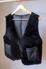 Chaleco reversible confeccionado en cuero genuino. Presenta un lado de piel de oveja gris con bolsillos de cuero negro y un lado de cuero liso gris. Diseño sin mangas con cierre frontal.