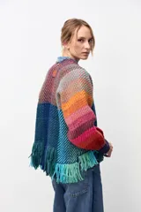 Chaqueta de tejido de punto con diseño multicolor a rayas diagonales en tonos cálidos y fríos. Presenta un panel frontal central en color azul sólido con flecos en el ruedo y puños tejidos en color violeta.