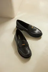 Mocasines negros de cuero con textura croco y detalle de logo VDM en dorado.