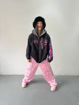 Campera reversible con cierre frontal. Un lado es de algodón negro con estampa y bordado en color rosa, y el otro lado es de tela polar de pelo largo en color gris. Presenta corte oversize, capucha y puños acanalados.