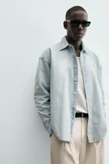 Camisa de denim de algodón, color celeste claro lavado, de corte relajado (relaxed fit) con cuello solapa, manga larga terminada en puño con botón y cierre frontal de botonadura. Presenta un pequeño bordado a contraste en el pecho.