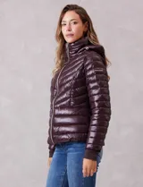 Campera puffer de acabado satinado en color marrón oscuro. Presenta un diseño capitoneado con líneas en V, cierre frontal metálico, capucha fija y puños internos de tejido elastizado con abertura para el pulgar. Incluye bolsillos laterales con cierre invisible y logo metálico en la manga.
