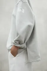 Buzo oversize color gris claro, con cuello redondo, hombros caídos y puños ajustados. Confeccionado con 50% algodón orgánico y 50% algodón reciclado.