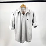 Camisa de vestir de algodón color gris claro con finas rayas verticales negras, cuello italiano, manga larga con puños abotonados y logo bordado en el pecho. Marca Duxon Originals.
