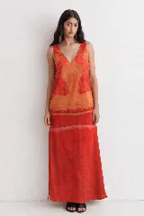 Vestido largo de silueta recta y caída fluida, con escote en V y breteles anchos. Presenta un estampado artístico en tonos rojos y naranjas.