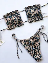 Conjunto de bikini con estampado animal print en tonos beige, negro y celeste. El corpiño es strapless con volados y abertura en el centro. La bombacha es tipo colaless con tiras ajustables en los laterales.