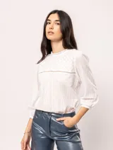 Blusa blanca de algodón con escote redondo, manga tres cuartos y silueta oversized. Presenta bordados y texturas combinadas.