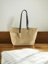 Bolso tipo tote de lona color beige con asas de cuero sintético negro, con hebilla decorativa. Tiene bolsillos laterales y es de gran capacidad.