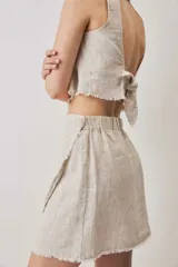Falda cruzada tipo wrap color beige, de lino, con diseño asimétrico y bordes deshilachados. Cuenta con cierre de botón en la cintura.