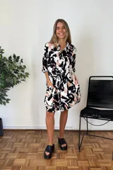 Camisa de manga larga con cuello y botones frontales, con un estampado abstracto en blanco, negro y rosado pálido. El corte es holgado y llega hasta medio muslo.