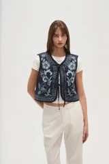 Chaleco sin mangas, color azul marino, con bordados florales en tono celeste claro. Presenta un escote en V y se cierra al frente con lazos ajustables.
