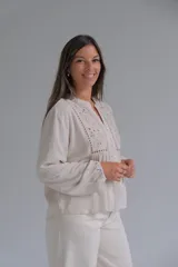Blusa de color beige con cuello mao y cierre frontal de botones. Presenta detalles de bordado floral y calados en el frente, con mangas largas de corte holgado.