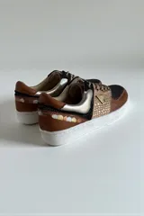 Championes de diseño urbano con combinación de tonos marrones, negros y detalles metalizados, puntera de cuero y suela blanca.