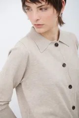 Cardigan de punto color beige, con cuello camisero, cierre frontal de botones y bolsillo aplicado en el pecho. Presenta mangas largas con puños acanalados y un corte recto y holgado.