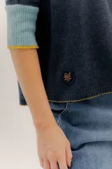 Buzo de punto en color negro con mangas tres cuartos y puños en contraste color marrón. Presenta un diseño holgado con tajos laterales y un aplique circular con logo en la parte inferior.