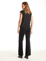 Blusa negra de punto elástico con caída fluida, cuello redondo y apliques de tachas doradas circulares en el cuello y los hombros. Tiene manga casquillo y ruedo redondeado.