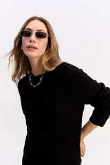 Buzo de punto negro con diseño de trenzas en relieve, cuello redondo y mangas largas.