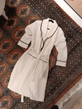 Bata de chambre larga color crudo, con cuello smoking y ribete negro. Incluye cinturón del mismo tejido y bolsillos laterales.