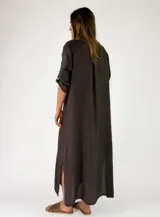 Vestido largo de lino color tostado, con diseño camisero, botonadura frontal completa con detalles de volados a lo largo de la botonadura, mangas largas arremangables y aberturas laterales en el bajo.