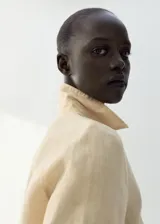 Camisa de lino color beige, de diseño recto con cuello camisero, manga larga con puños abotonados, bolsillo de parche en el pecho y cierre frontal de botones.