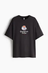 Remera oversized en punto suave de algodón de color negro con diseño estampado en el centro que muestra una taza de espresso y el texto "Quotidiana Delizia ROME". Cuenta con cuello redondo acanalado, hombros caídos y mangas cortas.