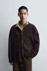 Cárdigan de punto negro con textura de canalé, cuello redondo y cierre frontal de botones.