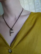 Collar de tiento de cuero marrón con dije en forma de letra y placa metálica con la inscripción de la marca.