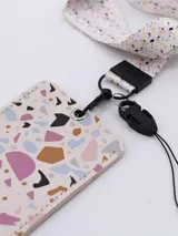 Tarjetero rectangular con estampado tipo terrazo en tonos pasteles, incluye cinta para colgar al cuello con diseño de puntos multicolor y gancho metálico.