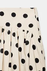 Falda pantalón de estilo globo con diseño abullonado y estampado de lunares negros sobre fondo crudo. Presenta cintura alta y cierre lateral con cremallera oculta.