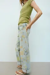 Jeans de tiro bajo y corte holgado, color celeste con estampado floral en tonos amarillos y verdes. Presenta diseño de cinco bolsillos, trabillas para cinturón y dobladillo con vuelta en los bajos. Cierre frontal con cremallera y botón metálico.