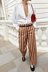 Pantalón de tiro alto y pernera recta con estampado de rayas verticales en tonos azul, marrón y beige. Incluye un cinturón delgado de color marrón oscuro con hebilla metálica dorada.