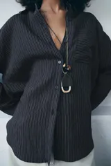 Camisa fluida de corte oversize confeccionada en mezcla de viscosa, con diseño de rayas verticales finas en tono beige sobre fondo blanco. Presenta cuello solapa, cierre frontal con botones, manga larga con puños y un bolsillo de plastrón en el pecho.