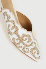 Zuecos color beige con bordado dorado de flores y pequeño tacón cuadrado.