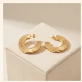 Aros tipo argolla de acero con baño de oro, con diseño texturizado de líneas verticales en relieve.
