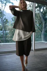 Jersey de punto color gris oscuro, con cuello alto y mangas anchas a tres cuartos. Presenta un bajo superpuesto de tejido satinado color crema o blanco roto.