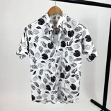 Camisa blanca estampada con hojas negras, de algodón 100%, cuello mao y manga corta.