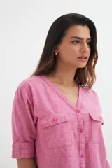 Camisa color blanco roto, de manga corta enrollada a 3/4, con escote en V y cierre frontal de botones. Presenta dos bolsillos de parche con solapa en el pecho.