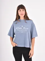 Remera de corte holgado y diseño oversize, color gris azulado con efecto lavado. Presenta un estampado gráfico central con tipografía y motivos florales.