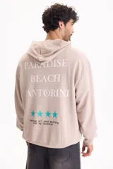 Buzo canguro con capucha color beige, con diseño estampado en la espalda que incluye el texto "Paradise Beach Santorini", cuatro estrellas celestes y la frase "working all year waiting for my vacation".