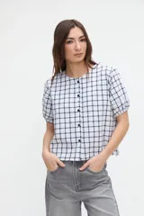 Camisa de manga corta abullonada, diseño a cuadros con base blanca y líneas oscuras, escote redondo y cierre frontal de botones.