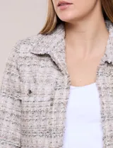 Chaqueta confeccionada en tejido de tweed beige con trama estructurada. Presenta cuello con solapa, frente abierto con botones metálicos y cuatro bolsillos funcionales. Las mangas largas de calce recto cuentan con bocamangas decoradas con botones y terminaciones deshilachadas al igual que los bordes.