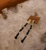 Aros colgantes marca Agnès, compuestos por una placa rectangular dorada en la parte superior y una cadena de piedras facetadas negras en la parte inferior.