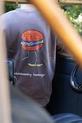 Buzo marrón con efecto lavado, cuello redondo y puños acanalados. Estampado en la espalda de una hamburguesa con piernas y una patineta, con la leyenda "skateboarding hamburger".