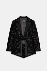 Blazer asimétrica negra de la línea ZW Collection, recubierta de lentejuelas tono sobre tono, con cuello solapa, manga larga y diseño cruzado con botones y cierre frontal con gancho metálico. Presenta bajo asimétrico con abertura y pliegues en la espalda.