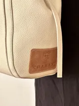 Bolso tipo tote de cuero color beige con doble asa de hombro y bolsillo externo con botón metálico.