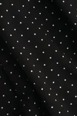 Vestido corto negro con estampado de lunares blancos, escote asimétrico de un solo hombro y tira ancha decorativa que cae desde el hombro.