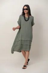 Vestido midi de lino color beige, de corte holgado y silueta acampanada. Cuenta con cuello redondo, mangas cortas amplias, bolsillos laterales y detalles de recortes horizontales en la falda con terminación asimétrica más larga en la parte trasera.