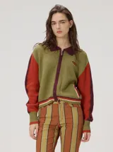 Campera estilo bomber de tejido de punto, diseño colorblock con cuerpo en verde militar, mangas rojas, cuello camisero y cierre frontal en bordó. Cuenta con puños y cintura elásticos a rayas, bolsillos laterales y parche bordado en el pecho.