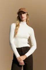 Polera de tejido acanalado al cuerpo, color blanco, con cuello alto y mangas largas con terminaciones onduladas en los puños.