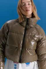 Campera puffer corta a la cintura, color verde militar con acabado brillante. Presenta cuello alto, cierre frontal completo y bolsillos laterales con cierre invisible.